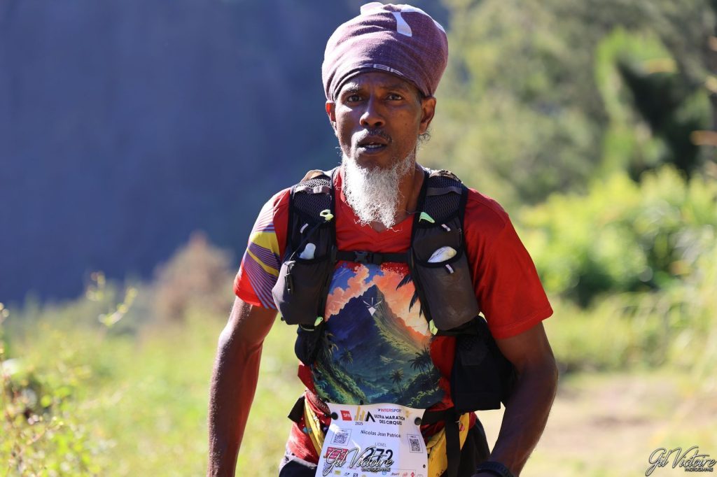 Coureur coiffé d’un turban, sac de trail sur le dos, sur un sentier ensoleillé
