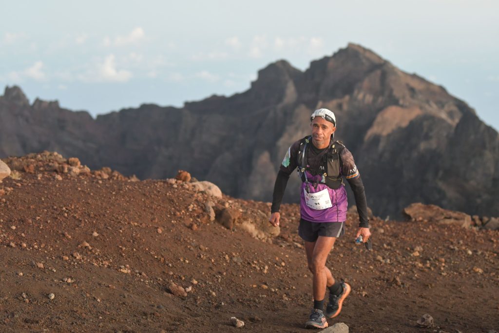 Coureur de l’Ultra Marathon des Cirques sur un sentier volcanique, sous un sommet rocheux